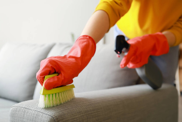 Frau putzt graues Sofa zu Hause mit Pinsel und Spülmittel, Nahaufnahme - Foto, Bild