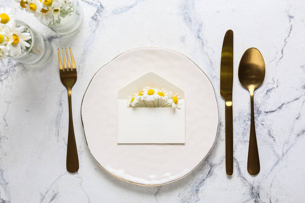 Beautiful table setting with wedding invitation and chamomile flowers on light background - Photo, Image