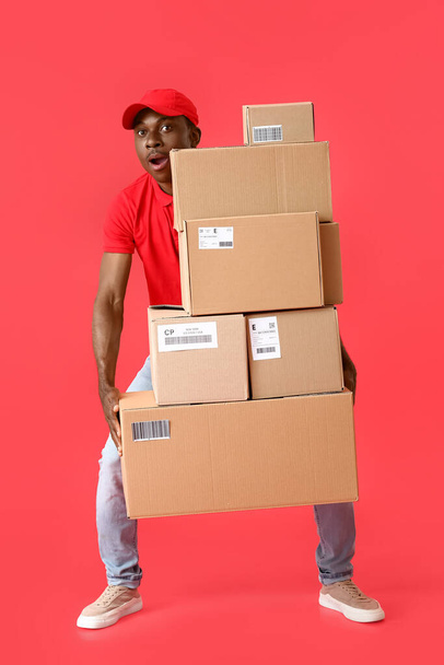 色の背景に多くの小包を持つアフリカ系アメリカ人の配達人 - 写真・画像