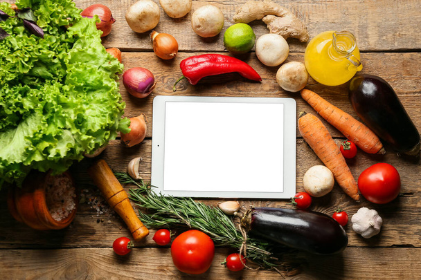 Tablet computer with tasty ingredients on wooden table - Photo, image