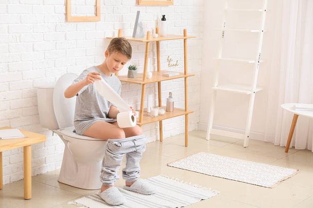 Маленький мальчик с бумагой сидит на унитазе в ванной комнате - Фото, изображение