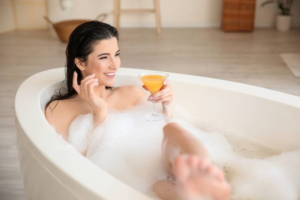 Pretty young woman taking relaxing bath with cocktail at home - Photo, Image