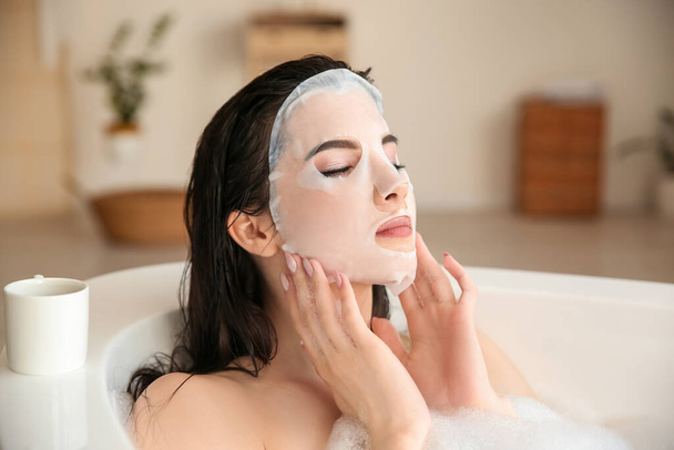 Pretty young woman with sheet facial mask taking bath at home - Fotoğraf, Görsel