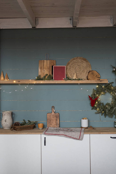 Minimalistyczne wnętrze domu z przytulnymi meblami kuchennymi, naczynia kuchenne, świąteczny wieniec na zakurzonej niebieskiej ścianie. Skandynawski hygge stylu Christmas decor - Zdjęcie, obraz