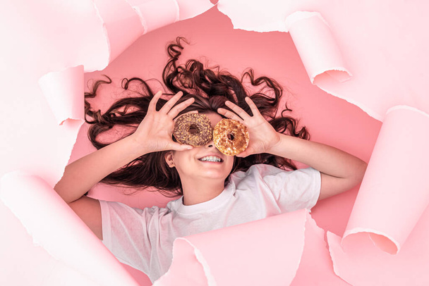 Веселая девушка с яркими пончиками на бумажном розовом фоне. - Фото, изображение