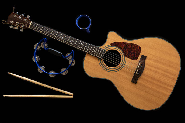 Acoustic guitar, drum sticks, tambourine and a cup on a black background. - Photo, Image