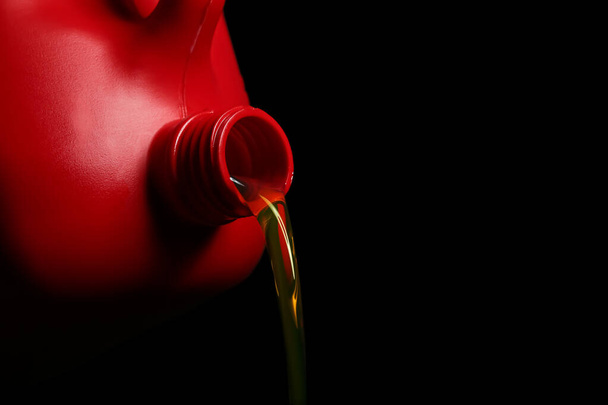 Pouring of motor oil from canister against black background - Фото, изображение