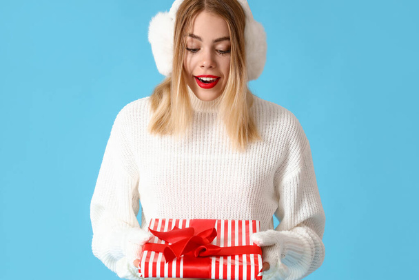Überraschte junge Frau mit Weihnachtsgeschenk auf blauem Hintergrund - Foto, Bild