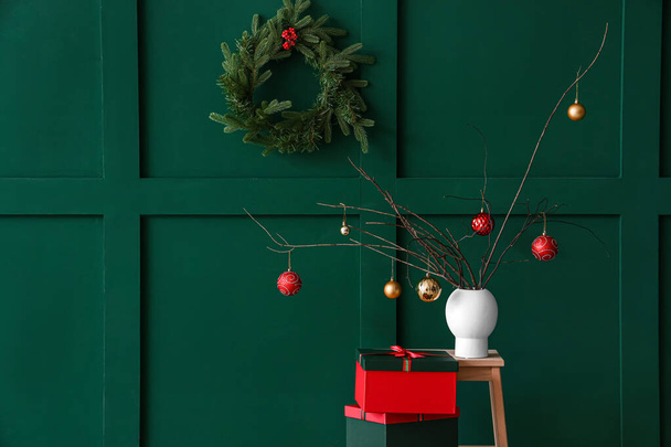 Baumzweige mit Weihnachtskugeln in Vase und Geschenken auf Leiter nahe grüner Mauer - Foto, Bild