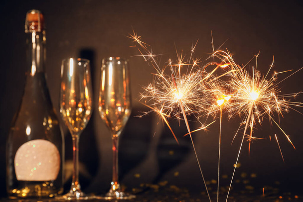 Wunderschöne Wunderkerzen, Gläser und eine Flasche Champagner auf dunklem Hintergrund - Foto, Bild