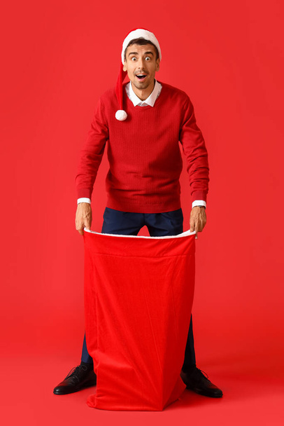 Surprised young man with Santa bag on red background - Photo, image
