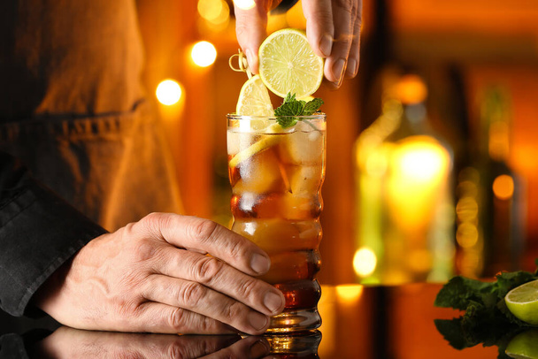 Male bartender squeezing lime in glass of tasty Cuba Libre cocktail on table in bar - Photo, Image