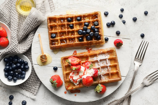 Wooden board of tasty Belgian Waffles with berries on light background - Photo, Image