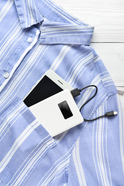 Modern power bank and mobile phone with shirt on white wooden background - Foto, Imagem