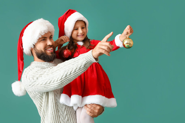 Niña y su padre en los sombreros de Santa y con adorno de Navidad en el fondo de color - Foto, imagen