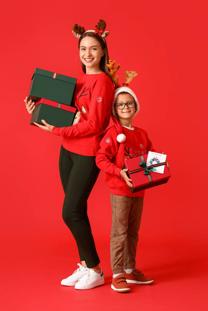 Little boy and his mother with Christmas gifts on color background - Fotó, kép