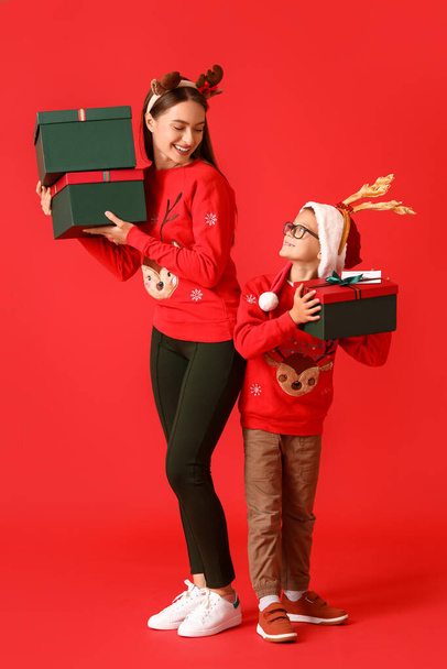 Little boy and his mother with Christmas gifts on color background - Foto, afbeelding