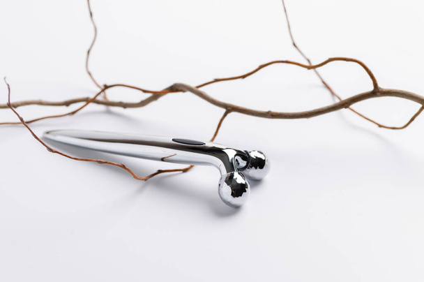 roller metal facial massager on white background, dry tree branch, beauty concept - Photo, Image