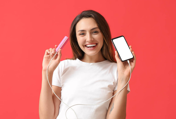 Young woman with phone and power bank on color background - Foto, immagini