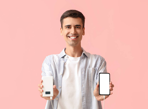 Young man with phone and power bank on color background - Photo, Image