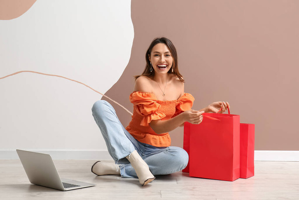 Mujer joven feliz con ordenador portátil y bolsas de compras en el fondo de color. Viernes Negro venta - Foto, imagen