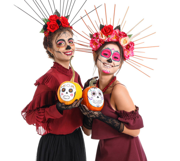 Stylish women with painted skull on faces and pumpkins against white background. Celebration of Mexico's Day of the Dead (El Dia de Muertos) - Photo, Image