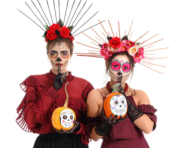 Mujeres elegantes con calavera pintada en rostros y calabazas mostrando gesto de silencio sobre fondo blanco. Celebración del Día de Muertos de México (El Día de Muertos)) - Foto, Imagen