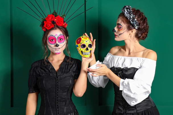 Stylové ženy s malovanými tvářemi a cukrovou lebkou na barevném pozadí. Oslava mexického Dne mrtvých (El Dia de Muertos) - Fotografie, Obrázek