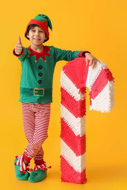 Lindo niño vestido como elfo con piñata de bastón de caramelo que muestra el pulgar hacia arriba en el fondo de color - Foto, imagen