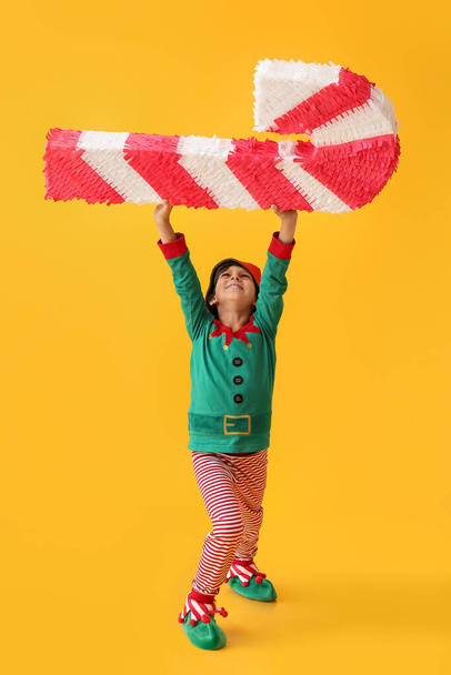 Lindo niño vestido como elfo con piñata de bastón de caramelo en el fondo de color - Foto, Imagen