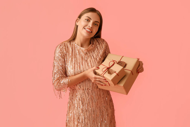 ピンクの背景にクリスマスの贈り物を持つ美しい若い女性 - 写真・画像