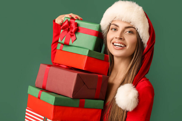 Hermosa joven en sombrero de Santa con regalos de Navidad sobre fondo verde - Foto, imagen