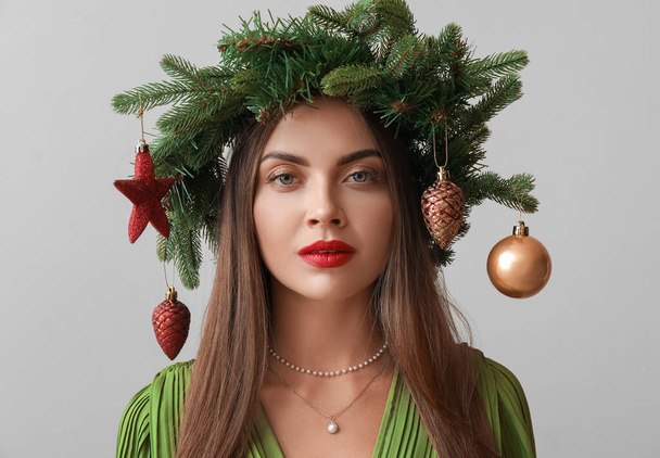 Hübsche junge Frau im Kranz mit Weihnachtsdekor auf beigem Hintergrund - Foto, Bild