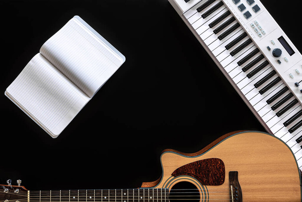 Musikhintergrund mit akustischer Gitarre, Notizblock und Musiktasten auf schwarz. - Foto, Bild