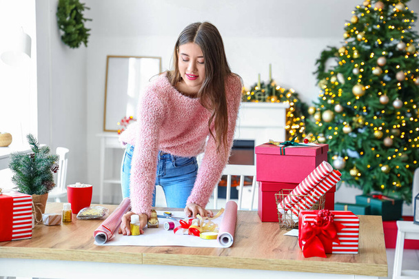 Beautiful young woman wrapping Christmas gift at home - Photo, Image