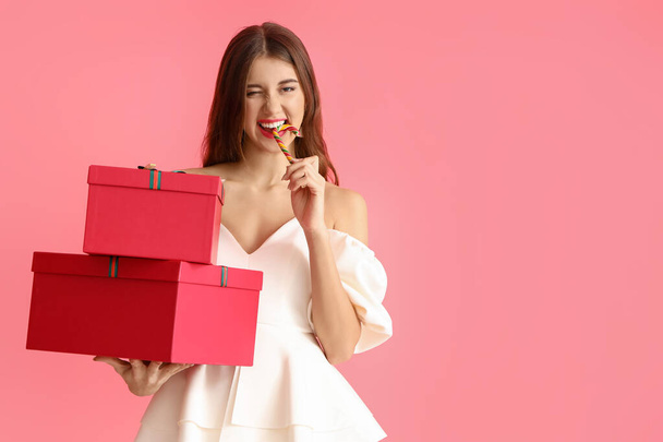 Beautiful young woman with Christmas gifts and candy cane on color background - Photo, Image