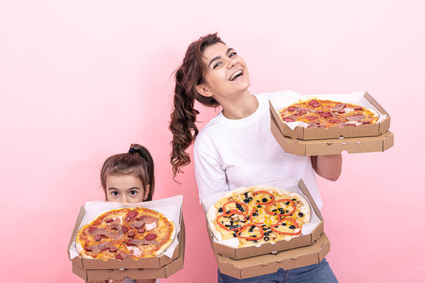 Взрослая девушка и маленькая девочка с коробками пиццы на розовом фоне. - Фото, изображение