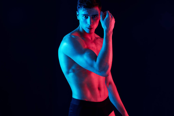sexy guy met atletische lichaamsbouw poseren op een zwarte achtergrond en houdt zijn hand in de buurt van zijn gezicht - Foto, afbeelding