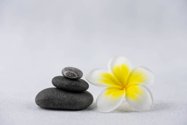 Pyramidy z šedého a bílého zenu oblázkové meditační kameny na bílém pozadí s plumeria tropické květiny. Koncept harmonie, rovnováhy a meditace, lázně, masáže, relax - Fotografie, Obrázek
