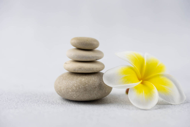 Pyramids of gray and white zen pebble meditation stones on white background with plumeria tropical flower. Concept of harmony, balance and meditation, spa, massage, relax - Photo, Image