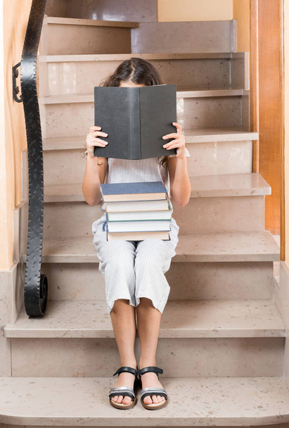 Uma rapariga nas escadas está a ler um livro. Vários livros jazem no colo. - Foto, Imagem