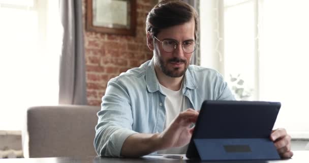 Serious millennial man sit at table using digital tablet - Séquence, vidéo