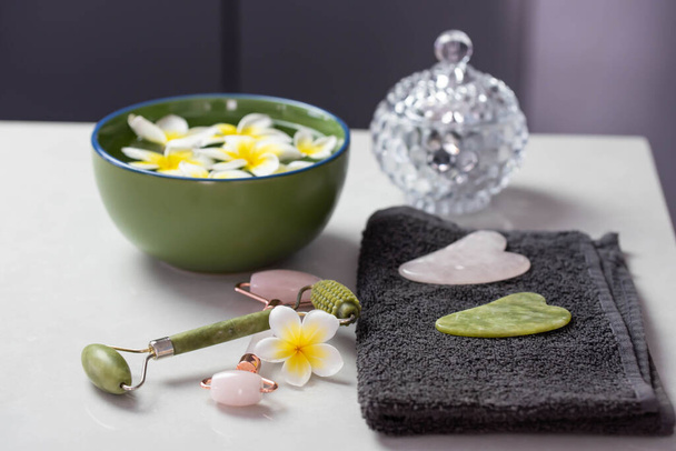 Beautiful spa composition with plumeria flowers. Face roller and guasha massager. Chinese Gua Sha massage tools. - Photo, Image