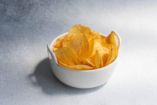 Хрустящие соленые картофельные чипсы или чипсы в миске на белом фоне. Концепция нездорового питания. - Фото, изображение