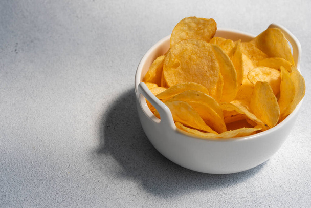 Хрустящие соленые картофельные чипсы или чипсы в миске на белом фоне. Концепция нездорового питания. - Фото, изображение