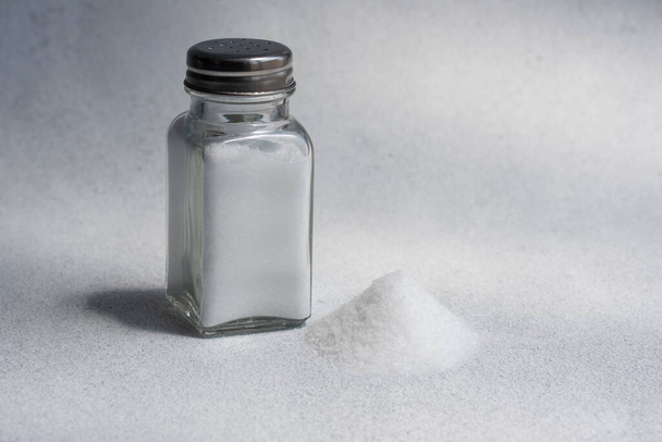 A pile of salt from salt shaker, word salt, concept excessive salt intake and white death  - Foto, afbeelding