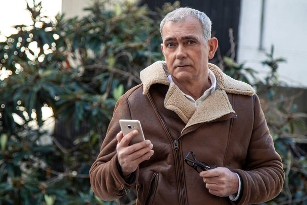 mature man in jacket using mobile phone on the street - Foto, Imagen