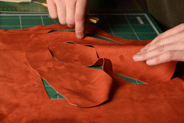 Ruce ševce držící řemeslný nůž řeže semišovou kůži pro ručně vyráběné boty na svém pracovišti v dílně. Detailní záběr. Selektivní zaměření - Fotografie, Obrázek