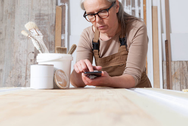 木工、携帯電話を持つ女性職人大工は、彼女のワークショップでインターネットを検索します。,復元,金型や手作りの作品のコンセプト - 写真・画像