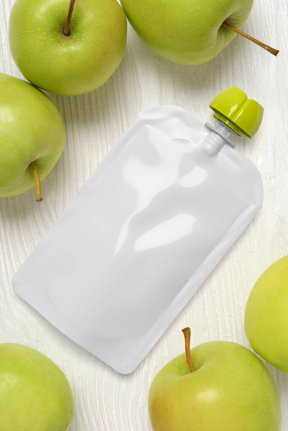 Weiße leere Plastiktüte für Babynahrung mit grünen Äpfeln auf einem Holztisch. Mock-up-Vorlage für Design. 3D-Darstellung. - Foto, Bild